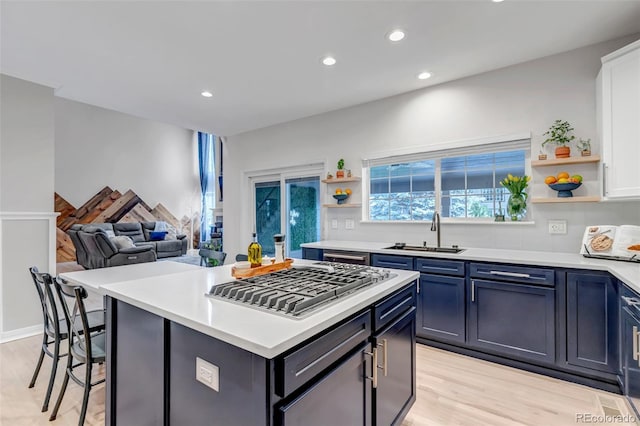 kitchen with open shelves, a sink, stainless steel gas cooktop, light wood-style flooring, and light countertops