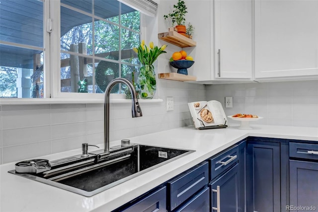 kitchen with open shelves, backsplash, blue cabinets, and a sink