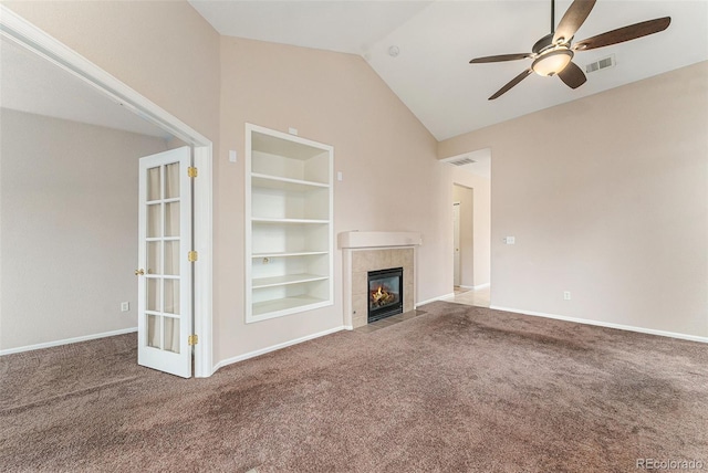 unfurnished living room featuring vaulted ceiling, built in features, ceiling fan, a tiled fireplace, and carpet