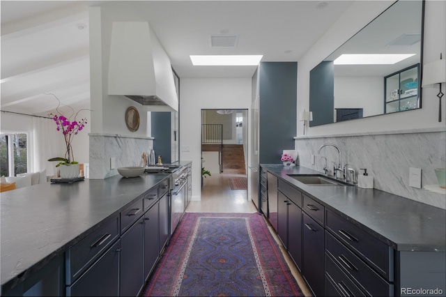 kitchen featuring backsplash, premium range hood, visible vents, and a sink