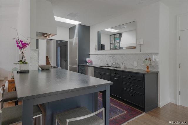 kitchen featuring a sink, stainless steel counters, a kitchen breakfast bar, wood finished floors, and tasteful backsplash