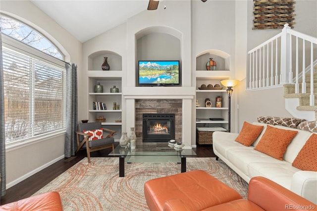 living room featuring a tiled fireplace, built in shelves, vaulted ceiling, and dark hardwood / wood-style floors