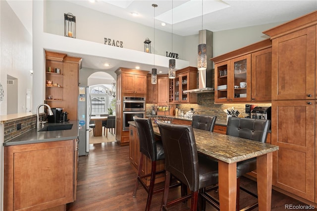 kitchen with pendant lighting, sink, wall chimney range hood, a kitchen bar, and decorative backsplash