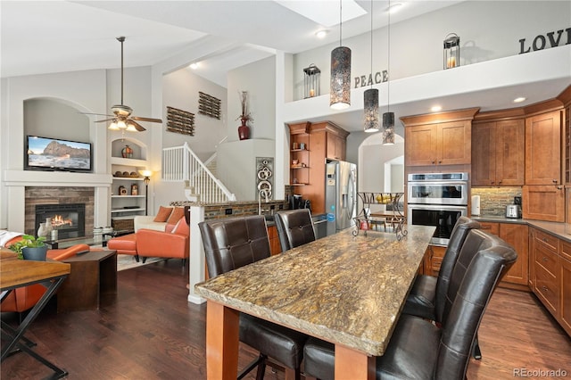 dining room featuring ceiling fan, dark hardwood / wood-style floors, a high ceiling, built in shelves, and a stone fireplace