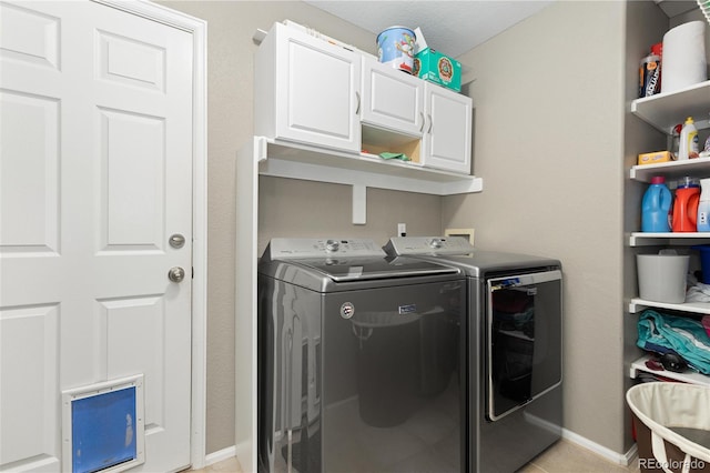 clothes washing area featuring cabinets, washing machine and dryer, and light tile patterned flooring