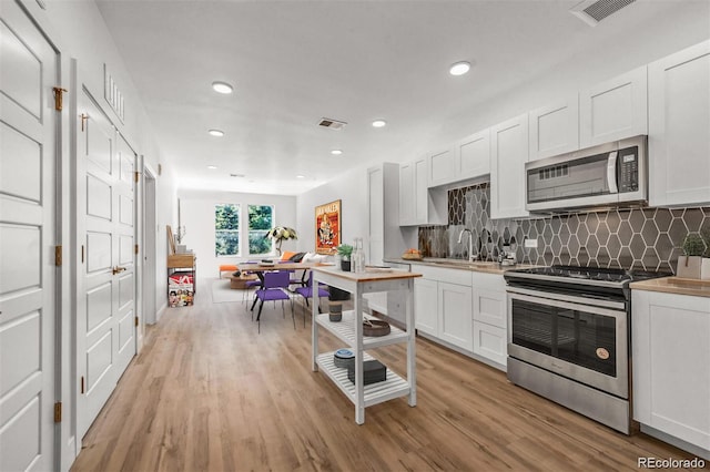 kitchen with white cabinets, sink, stainless steel appliances, and light hardwood / wood-style flooring