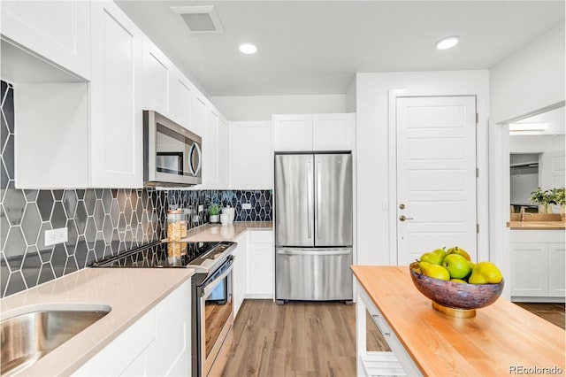 kitchen with decorative backsplash, white cabinetry, appliances with stainless steel finishes, and light hardwood / wood-style flooring