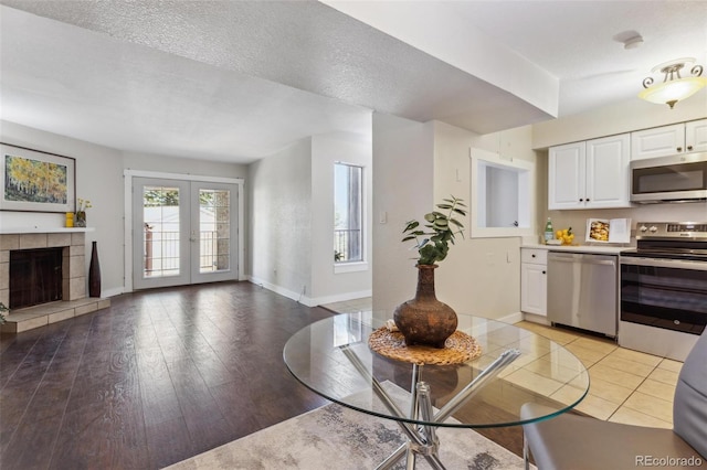 living room with french doors, baseboards, light wood-type flooring, and a fireplace