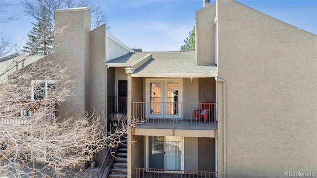view of side of home with stucco siding, a chimney, stairway, french doors, and a shingled roof
