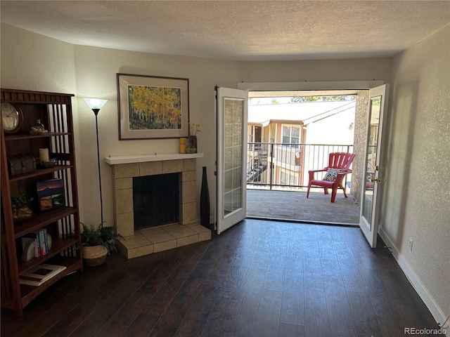 living area with a textured ceiling, a tile fireplace, a textured wall, and hardwood / wood-style flooring