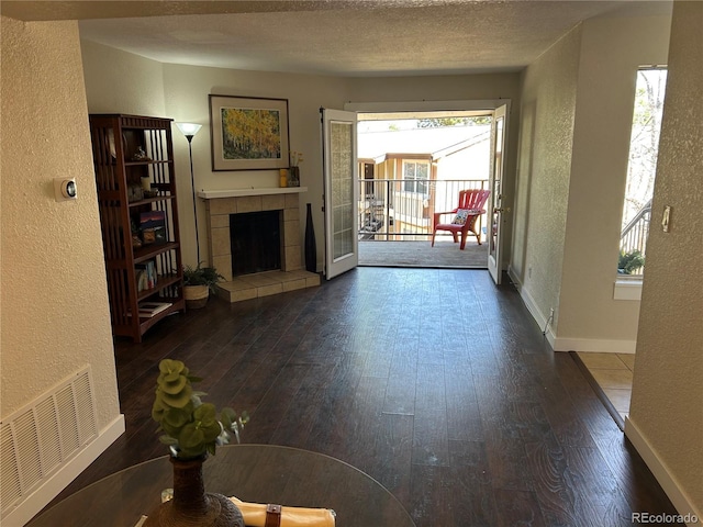 unfurnished living room featuring a textured wall, wood-type flooring, visible vents, and a fireplace