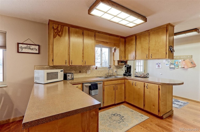 kitchen featuring a peninsula, white microwave, a sink, and stainless steel dishwasher