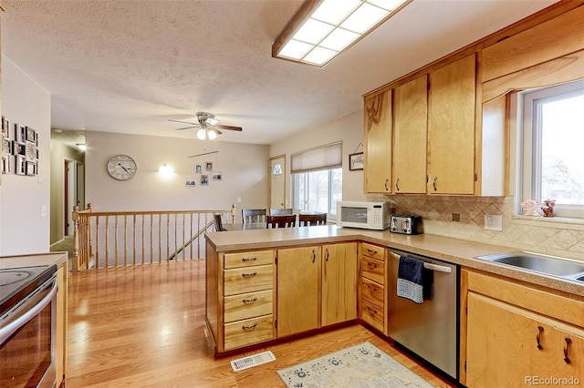 kitchen with a peninsula, visible vents, appliances with stainless steel finishes, backsplash, and light wood finished floors