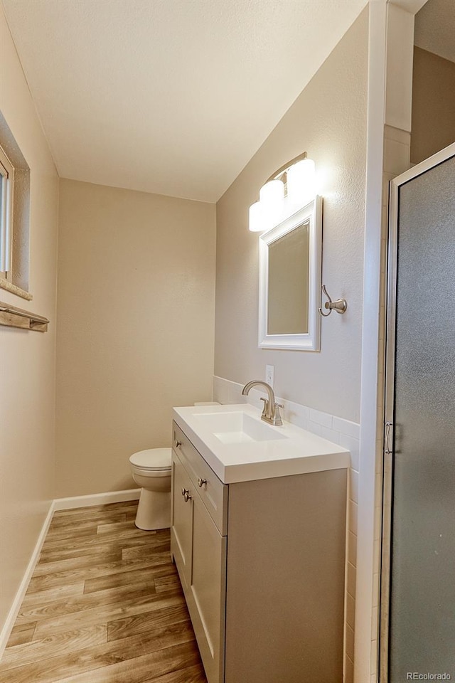 bathroom featuring toilet, a shower stall, vanity, wood finished floors, and baseboards