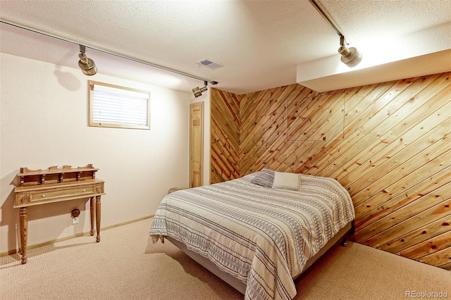 bedroom featuring carpet floors, visible vents, wood walls, a textured ceiling, and track lighting