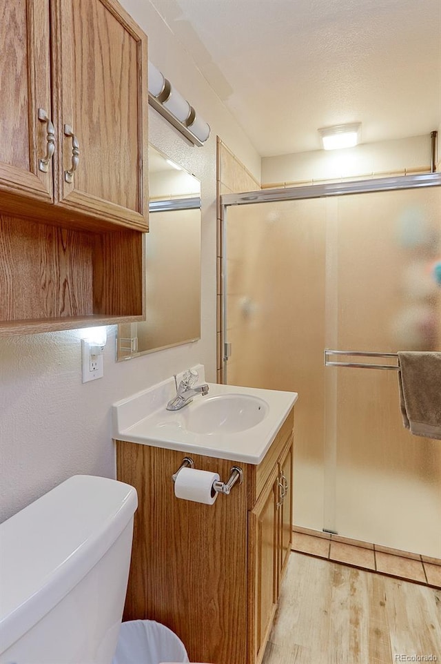 bathroom featuring toilet, a stall shower, wood finished floors, and vanity