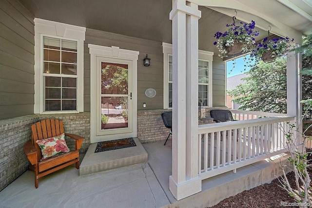 view of exterior entry featuring covered porch and brick siding