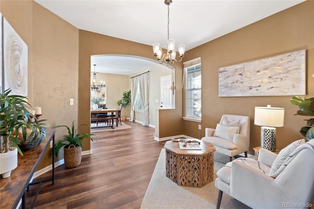 living area with baseboards, arched walkways, a notable chandelier, and wood finished floors