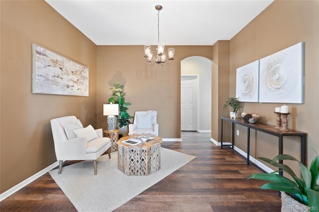 living area featuring arched walkways, dark wood-style flooring, a notable chandelier, and baseboards