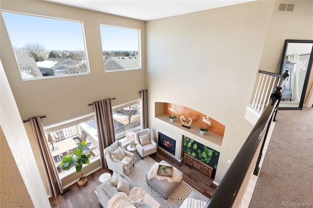 living area featuring a towering ceiling, wood finished floors, a glass covered fireplace, and visible vents