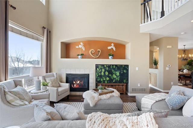 living area featuring visible vents, a tile fireplace, a towering ceiling, wood finished floors, and an inviting chandelier