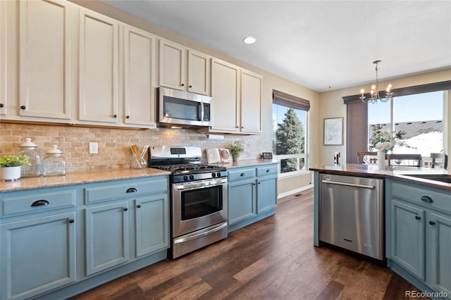 kitchen featuring dark wood-style flooring, blue cabinets, a notable chandelier, stainless steel appliances, and backsplash