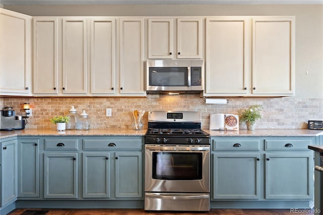 kitchen with appliances with stainless steel finishes, blue cabinetry, light stone counters, and tasteful backsplash