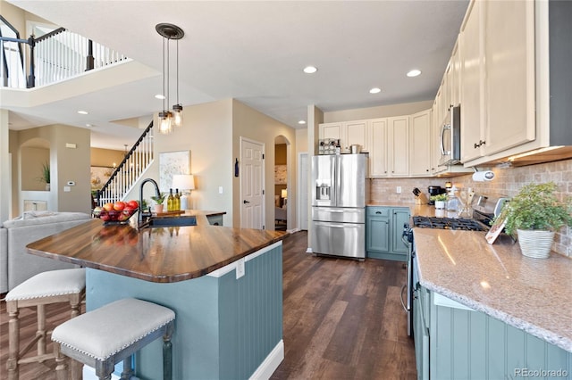 kitchen with arched walkways, a sink, wood counters, open floor plan, and appliances with stainless steel finishes