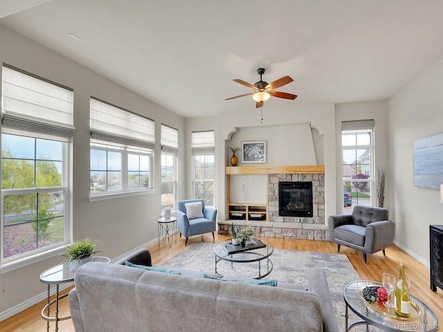 living area with baseboards, ceiling fan, a stone fireplace, and wood finished floors