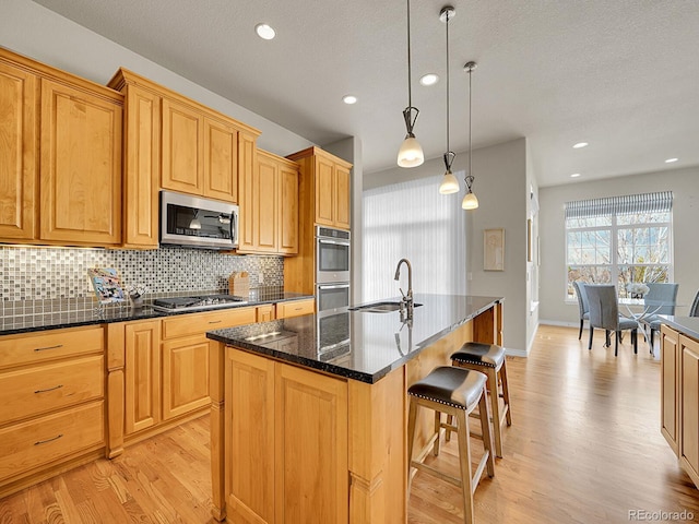 kitchen with a breakfast bar, a sink, light wood finished floors, stainless steel appliances, and decorative backsplash