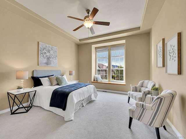 carpeted bedroom with a tray ceiling, ceiling fan, and baseboards
