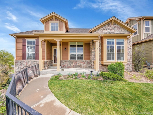 view of front of property with a porch, a front yard, and stone siding
