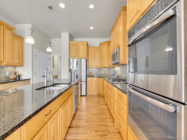 kitchen featuring tasteful backsplash, a sink, light wood-style flooring, appliances with stainless steel finishes, and hanging light fixtures