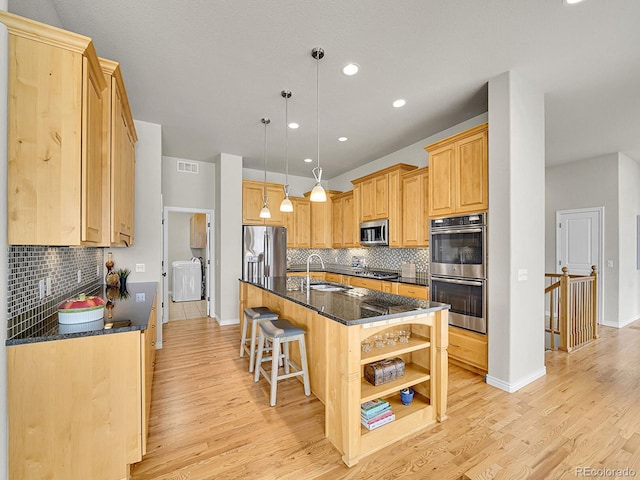 kitchen with dark stone counters, tasteful backsplash, a sink, light wood finished floors, and stainless steel appliances