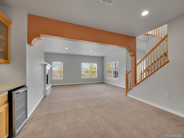 unfurnished living room featuring light colored carpet, stairway, baseboards, beverage cooler, and recessed lighting