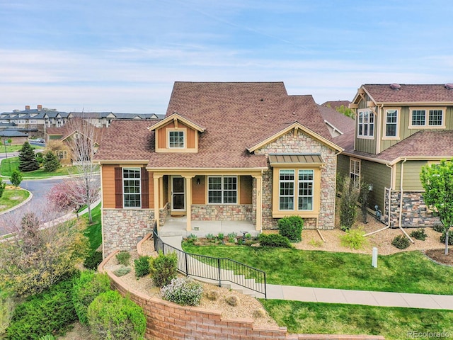 view of front of home with a shingled roof, a porch, a front lawn, and stone siding