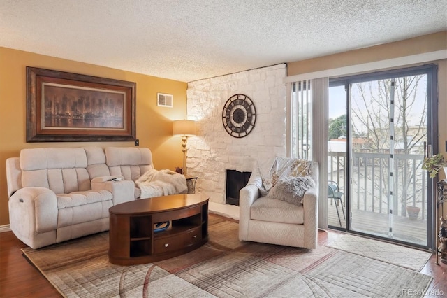 living area with visible vents, a textured ceiling, a stone fireplace, and wood finished floors