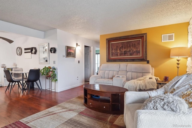 living area with a textured ceiling, a ceiling fan, visible vents, wood finished floors, and baseboards