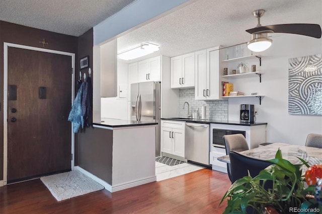 kitchen featuring light wood-style flooring, dark countertops, white cabinets, appliances with stainless steel finishes, and a sink