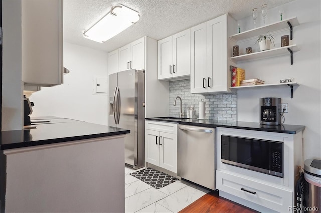 kitchen featuring white cabinets, appliances with stainless steel finishes, marble finish floor, a sink, and dark countertops