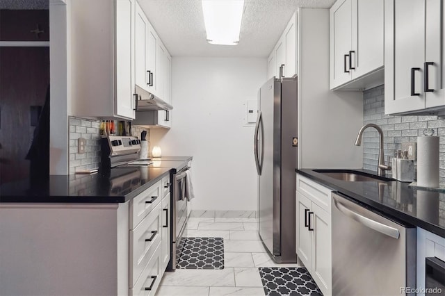 kitchen with under cabinet range hood, marble finish floor, dark countertops, a sink, and stainless steel appliances