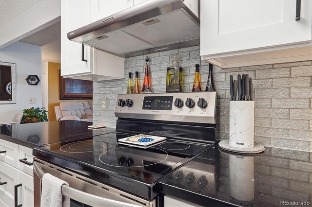 kitchen featuring white cabinetry, under cabinet range hood, dark stone counters, decorative backsplash, and electric stove