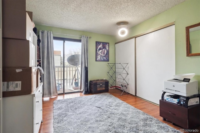bedroom with a closet, access to exterior, a textured ceiling, and wood finished floors
