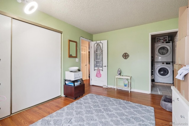 bedroom featuring stacked washing maching and dryer, a closet, a textured ceiling, and wood finished floors
