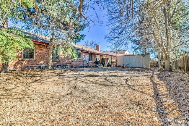 back of house featuring a chimney, fence, a storage unit, an outdoor structure, and brick siding