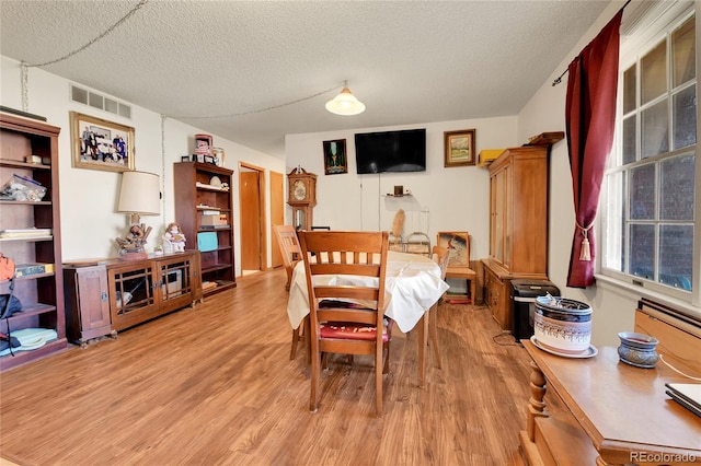 dining area with light wood-type flooring, visible vents, and a textured ceiling