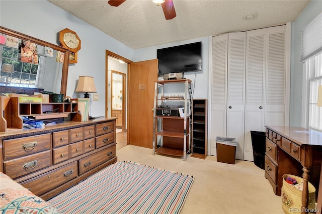 bedroom with a closet, light colored carpet, ceiling fan, and a textured ceiling