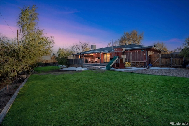 back house at dusk featuring a playground and a lawn