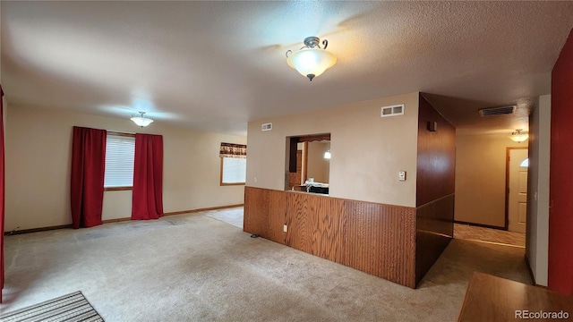 interior space featuring light carpet, wooden walls, and a textured ceiling