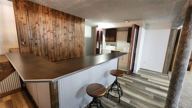 bar featuring light hardwood / wood-style flooring, washer and clothes dryer, a textured ceiling, and wood walls